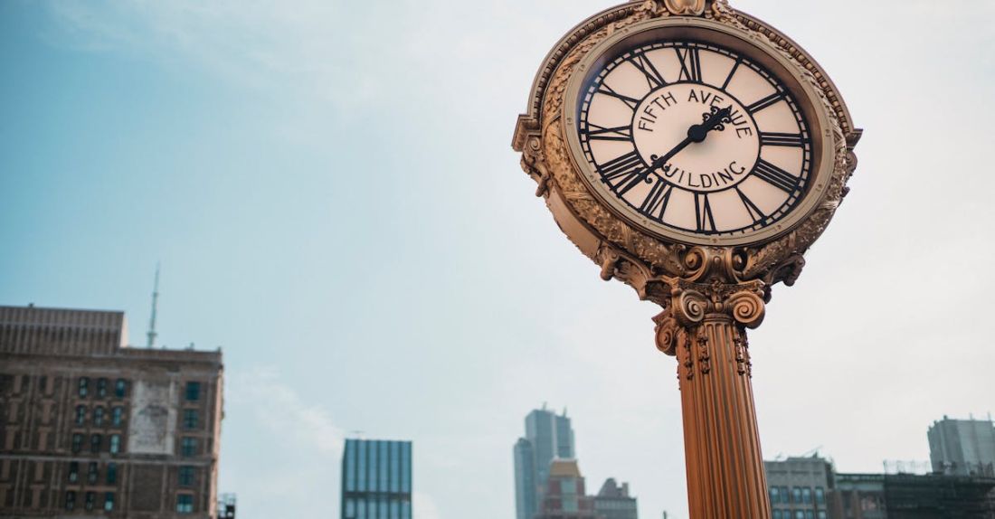 Time Blocking - From below of aged metal clock tower located in city center with high towers