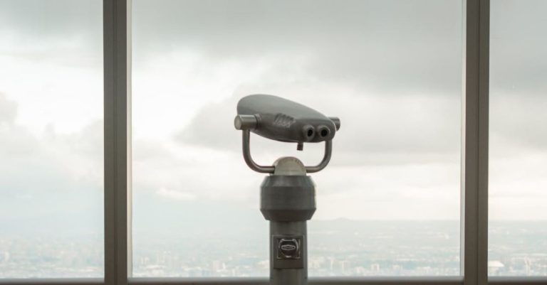 Desk Height - Modern stationary city binoculars near glass wall of high building to observe contemporary cityscape